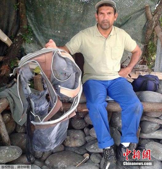 圖為當(dāng)?shù)貢r間7月30日，留尼旺島上的一名海岸清潔人員展示他找到的一個手提箱的殘骸。